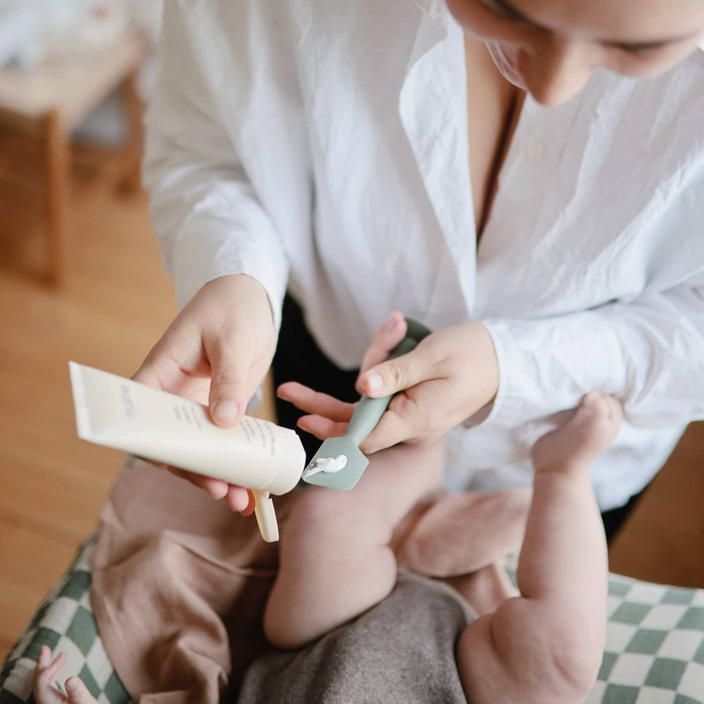 Mushie soft silicone diaper cream applicator being used on a baby