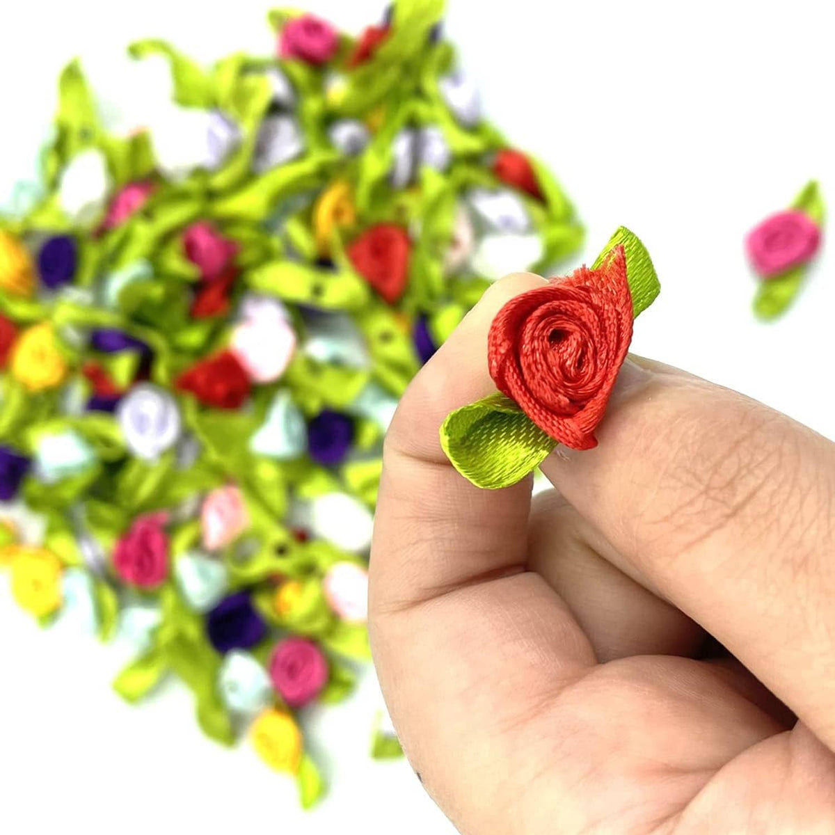 Hand holding a mini fabric ribbon rose with green leaves from a colorful bundle