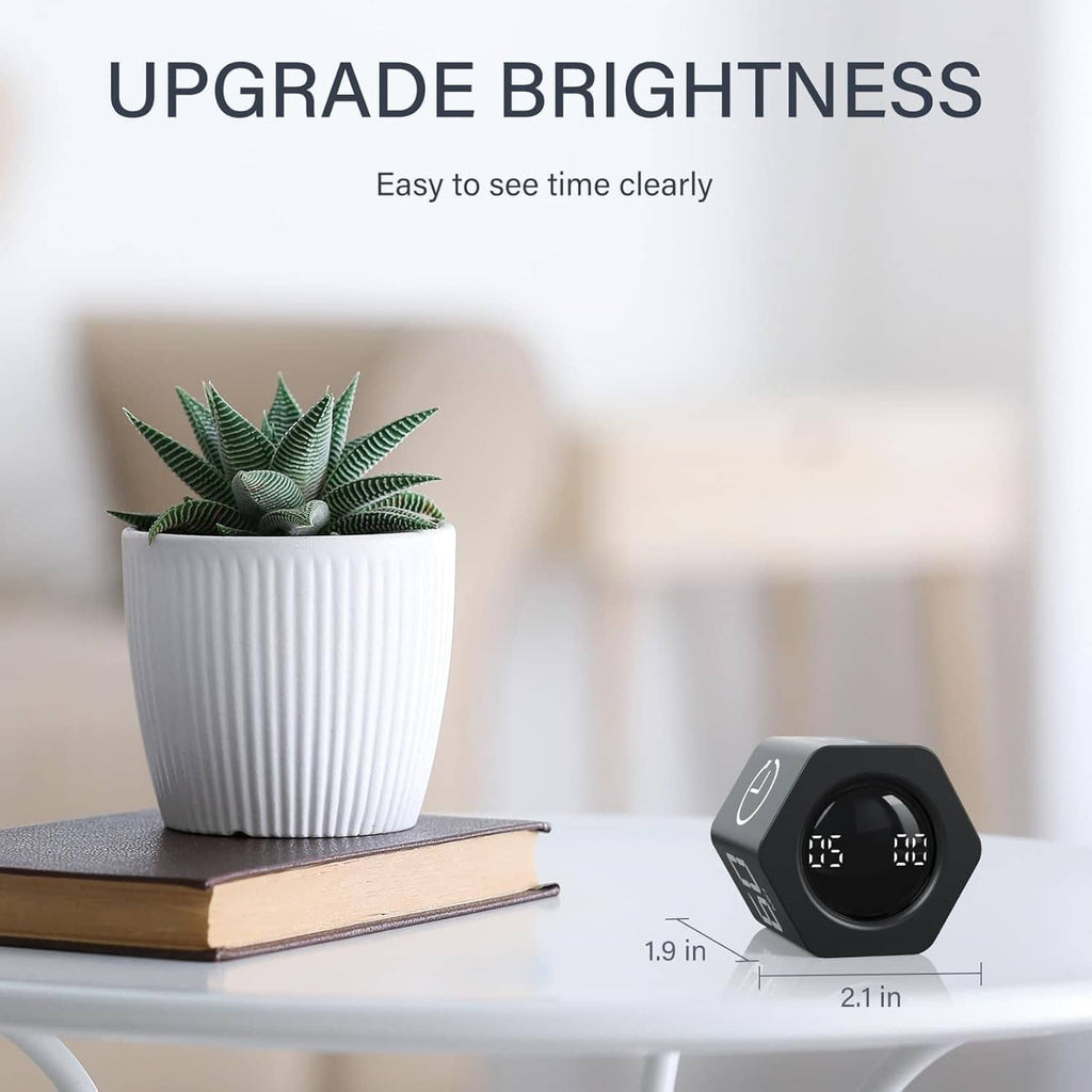 Black rotating timer with bright digital display on a desk beside a potted plant