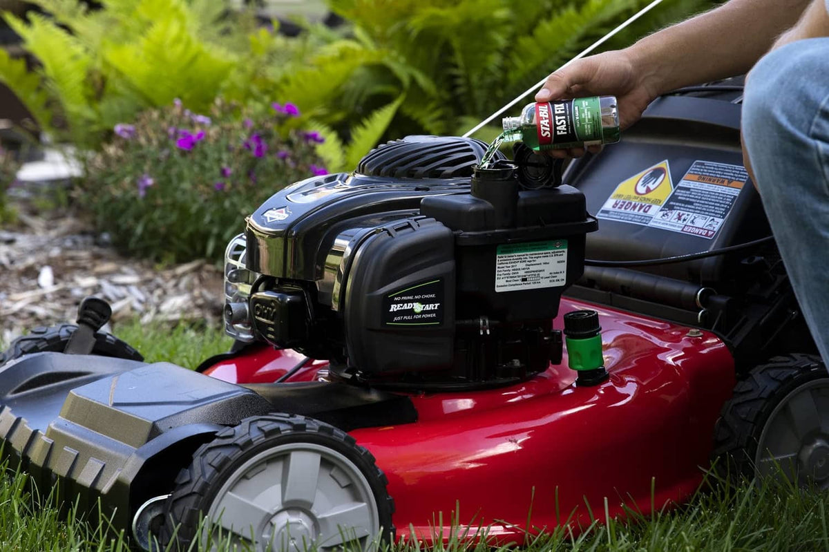 Person holding STA-BIL Fast Fix bottle while adding to a gas mower engine