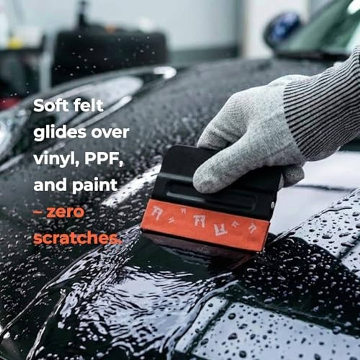 Squeegee tool with orange felt edge gliding over wet car surface; black blade visible.