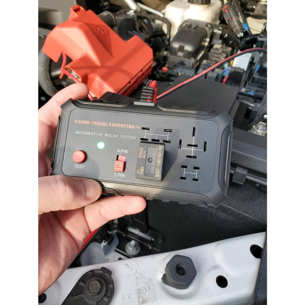 Automotive relay tester held in hand near car relay panel with red fuse insert