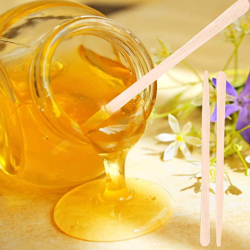 Eyebrow wax applicator stick dipped in amber wax with two wooden tools