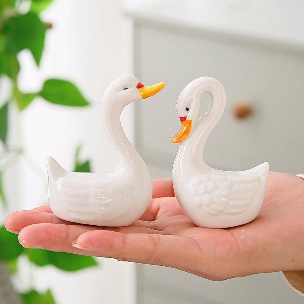 Two white ceramic swan figurines with orange beaks held in a hand