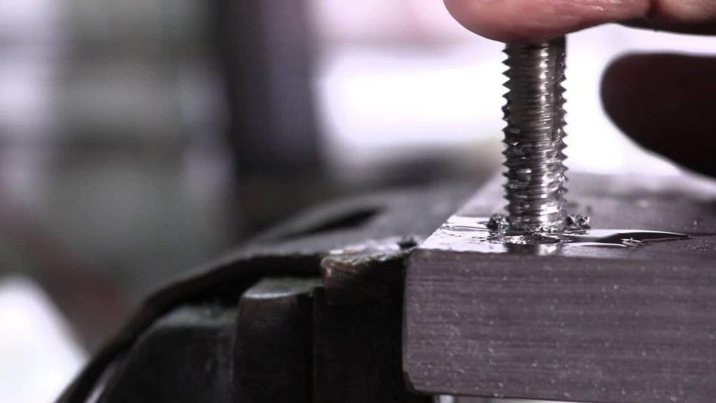 Tap cutting threads into a metal workpiece in close-up