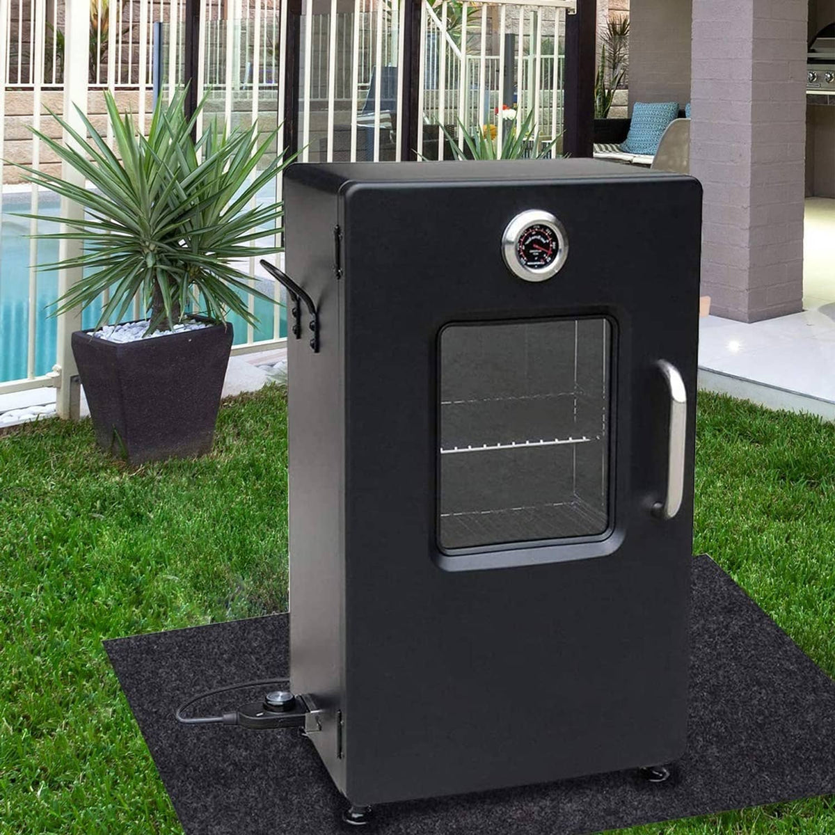Dark gray grill mat placed under a grill on outdoor grass