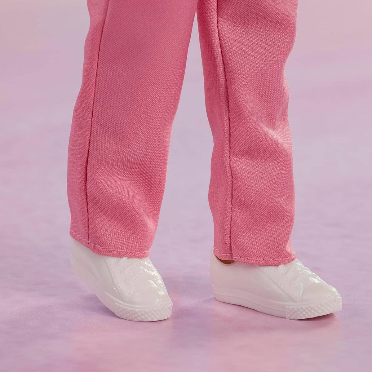 Collectible doll legs wearing pink pants with stitched seams and white sneakers