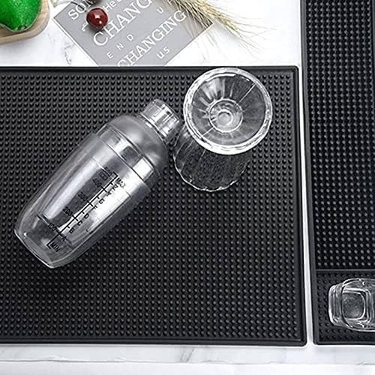 Black rubber bar mat with raised dot texture, holding a bottle and clear cup
