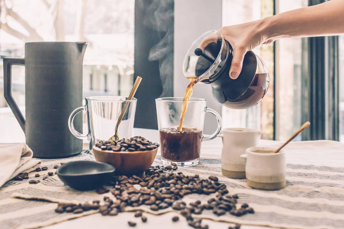 Coffee beans scattered on table with cups and brewing tools