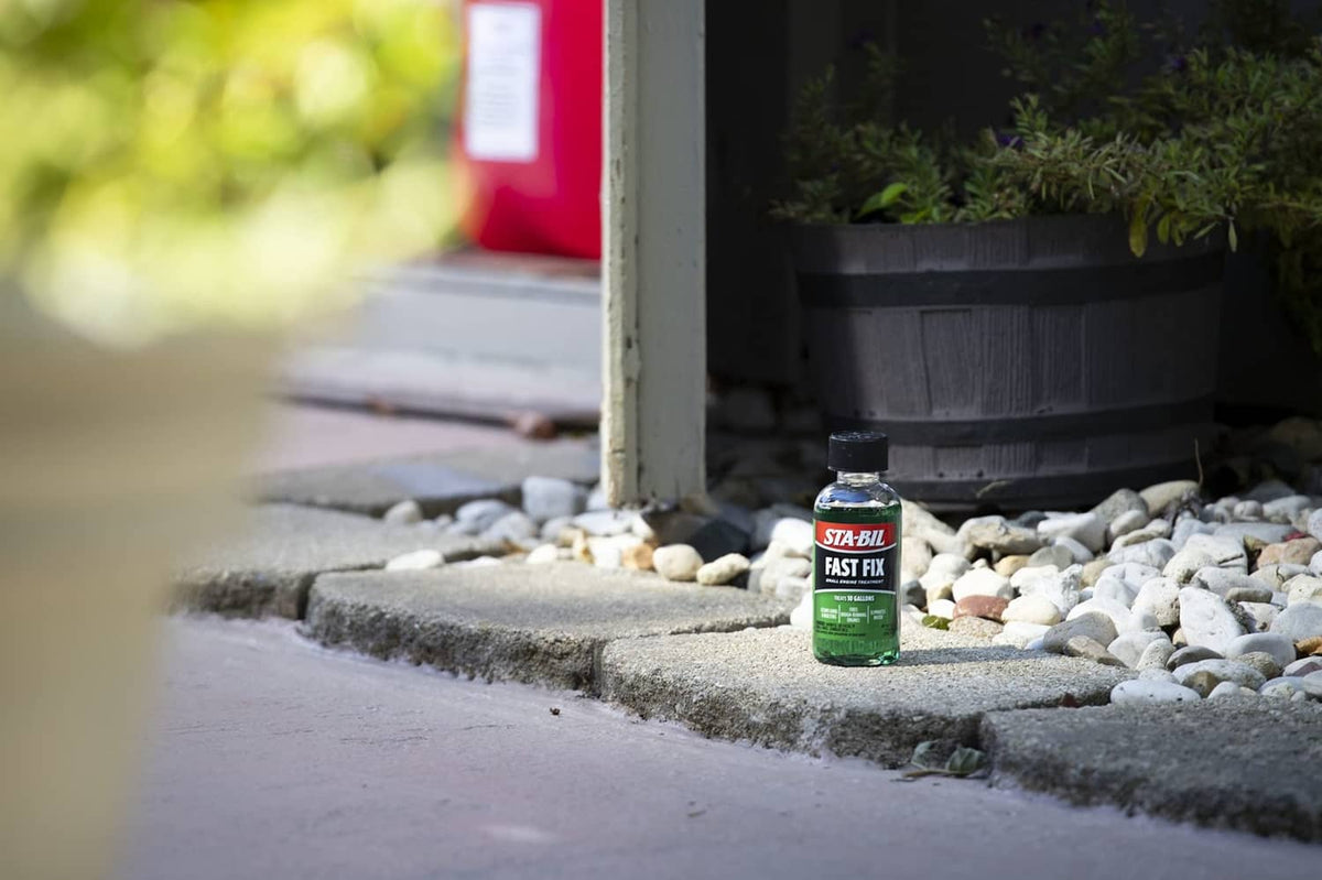 STA-BIL Fast Fix small engine treatment bottle placed on rocks near a patio