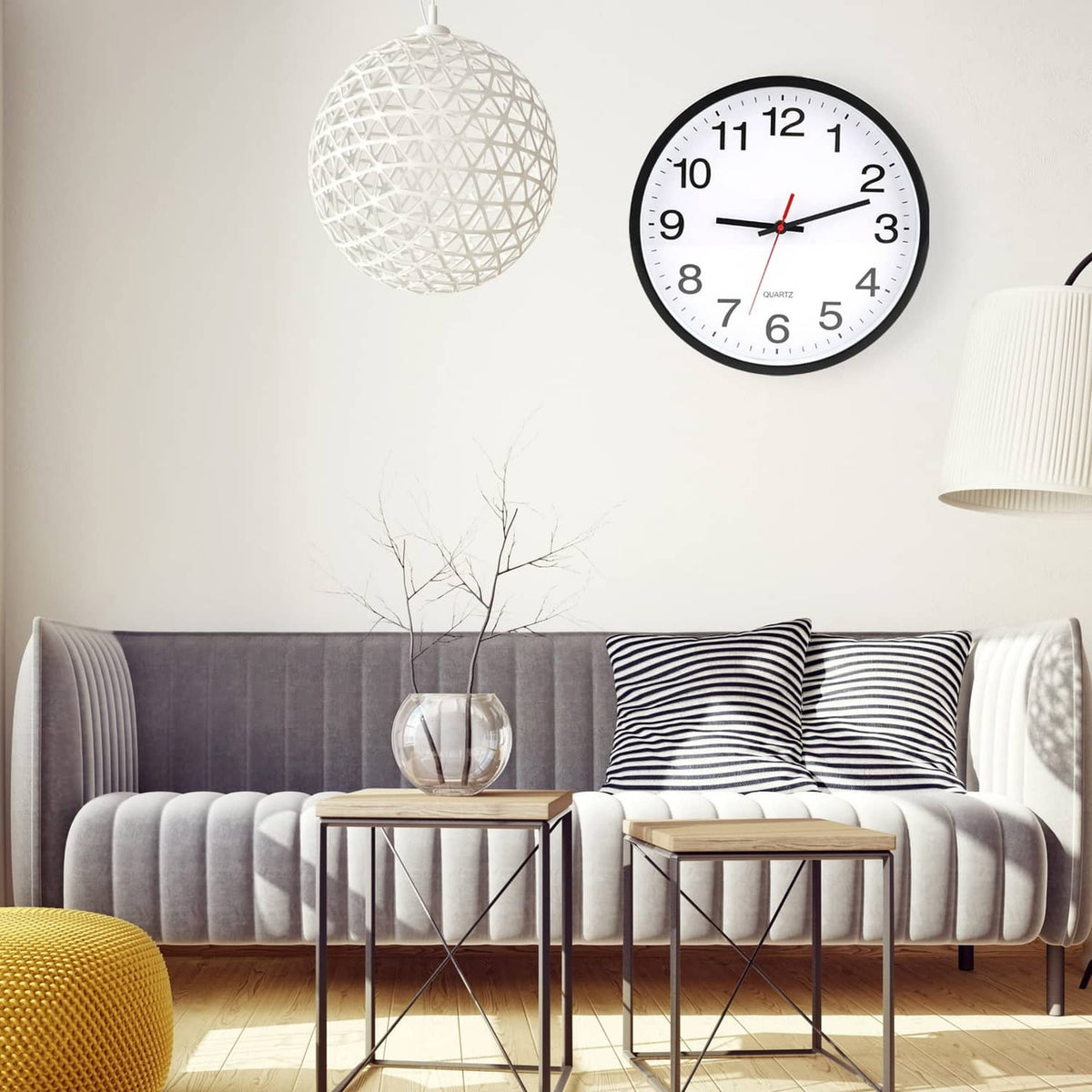 Round black wall clock with white dial, black numerals, and red hands in living room.