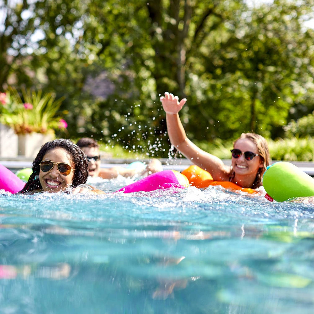 Pool noodle floats in water: orange with pink and green ends.
