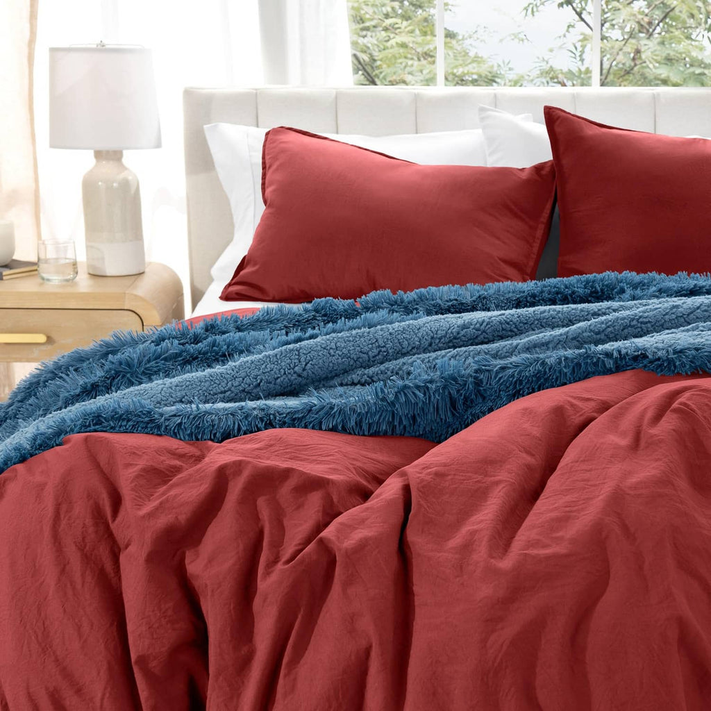 Red duvet cover set with two pillow shams beneath a blue shag throw