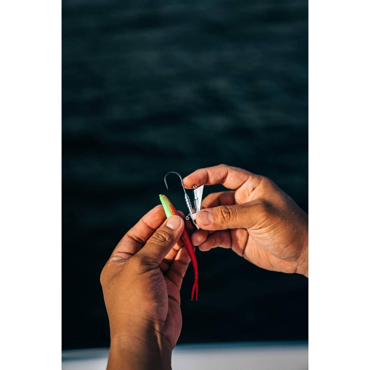 Red-green fishing lure with metal hook and red tail held between fingers