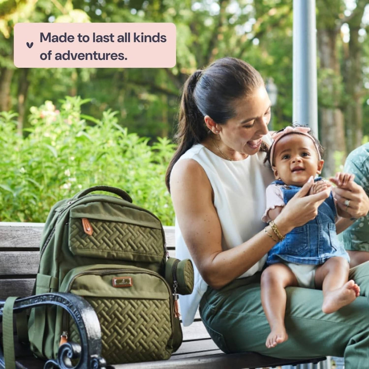 Olive green quilted diaper bag backpack outdoors with baby sitting beside