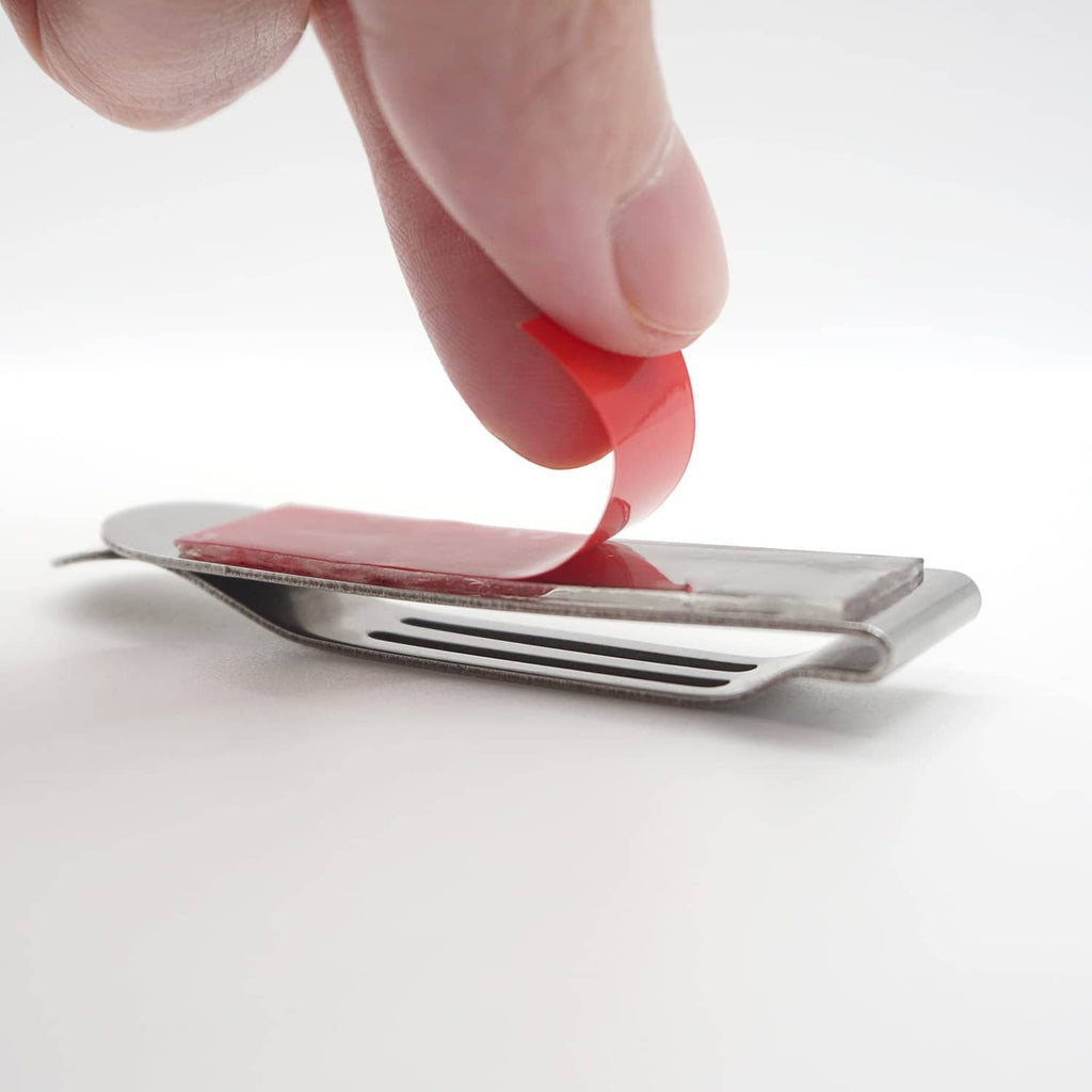 Silver pocket clip being pressed onto a phone edge with red backing