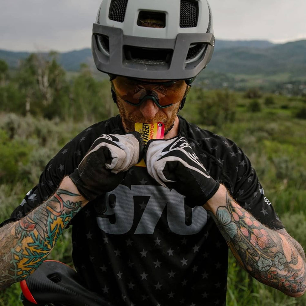 Cyclist holding Honey Stinger energy gel packet to mouth with helmet and goggles