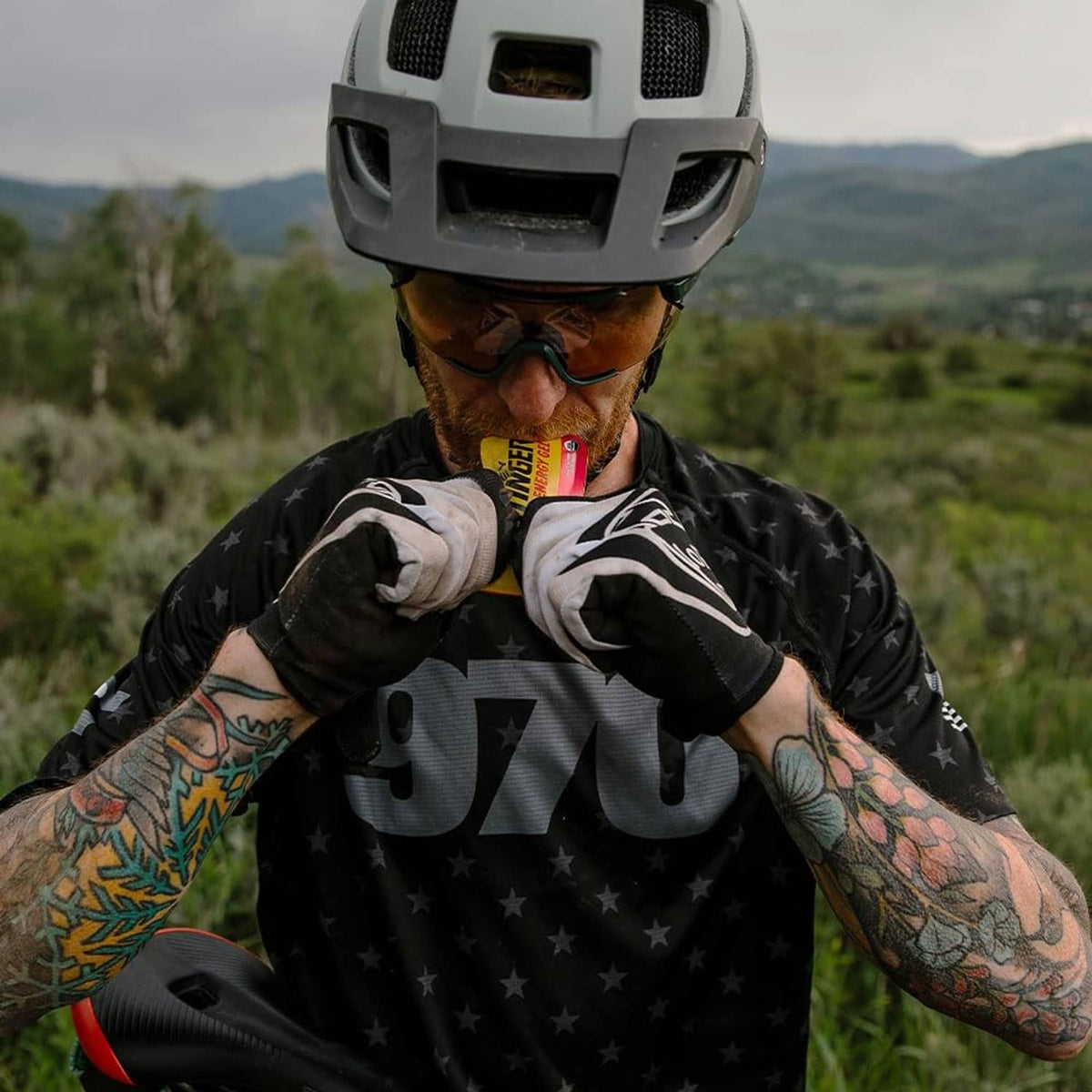 Cyclist holding Honey Stinger energy gel packet to mouth with helmet and goggles