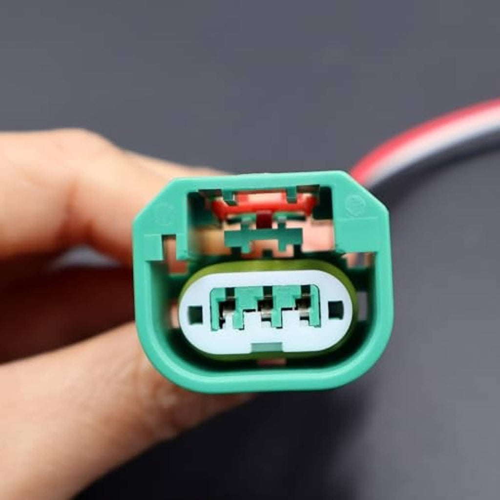 Green headlight connector socket with visible internal contacts; red/black wire leads