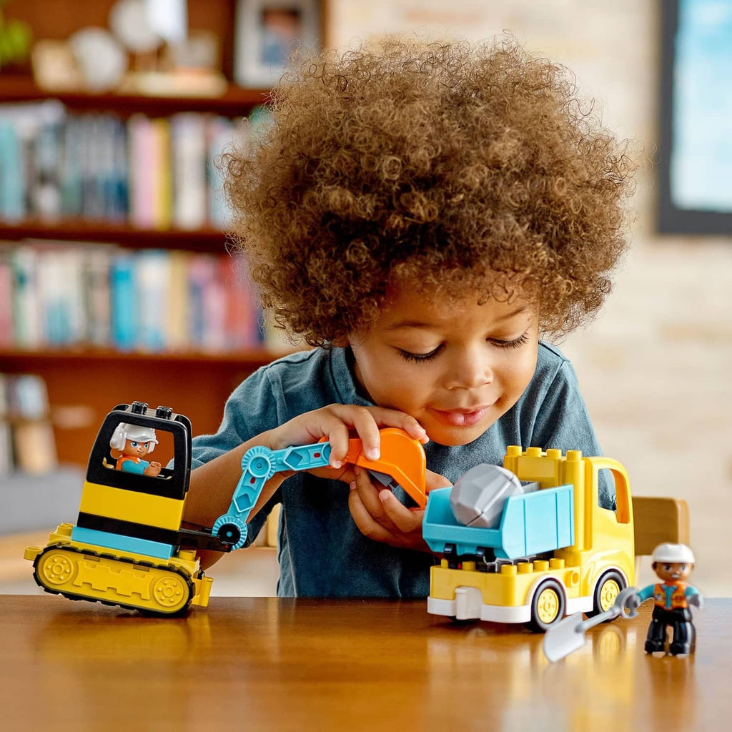 Child playing with yellow and blue LEGO DUPLO construction truck and tracked excavator toys