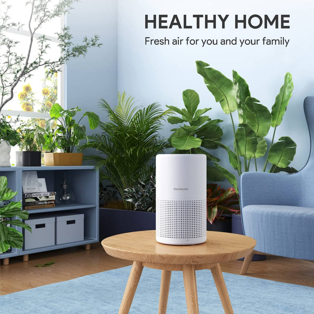 White air purifier on a round wooden table with front intake grille and top controls