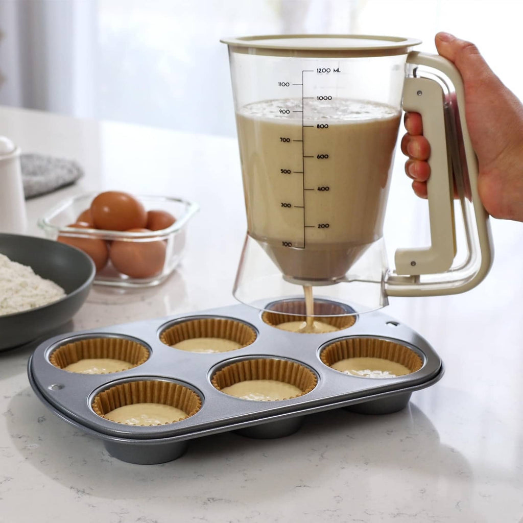 Beige 5-cup batter dispenser in hand, pouring batter over muffin pan cups