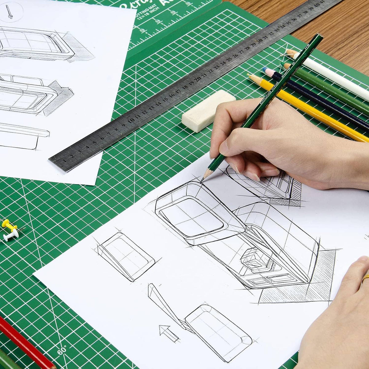 Green cutting mat with grid lines beside sketch paper and a hand holding a pencil