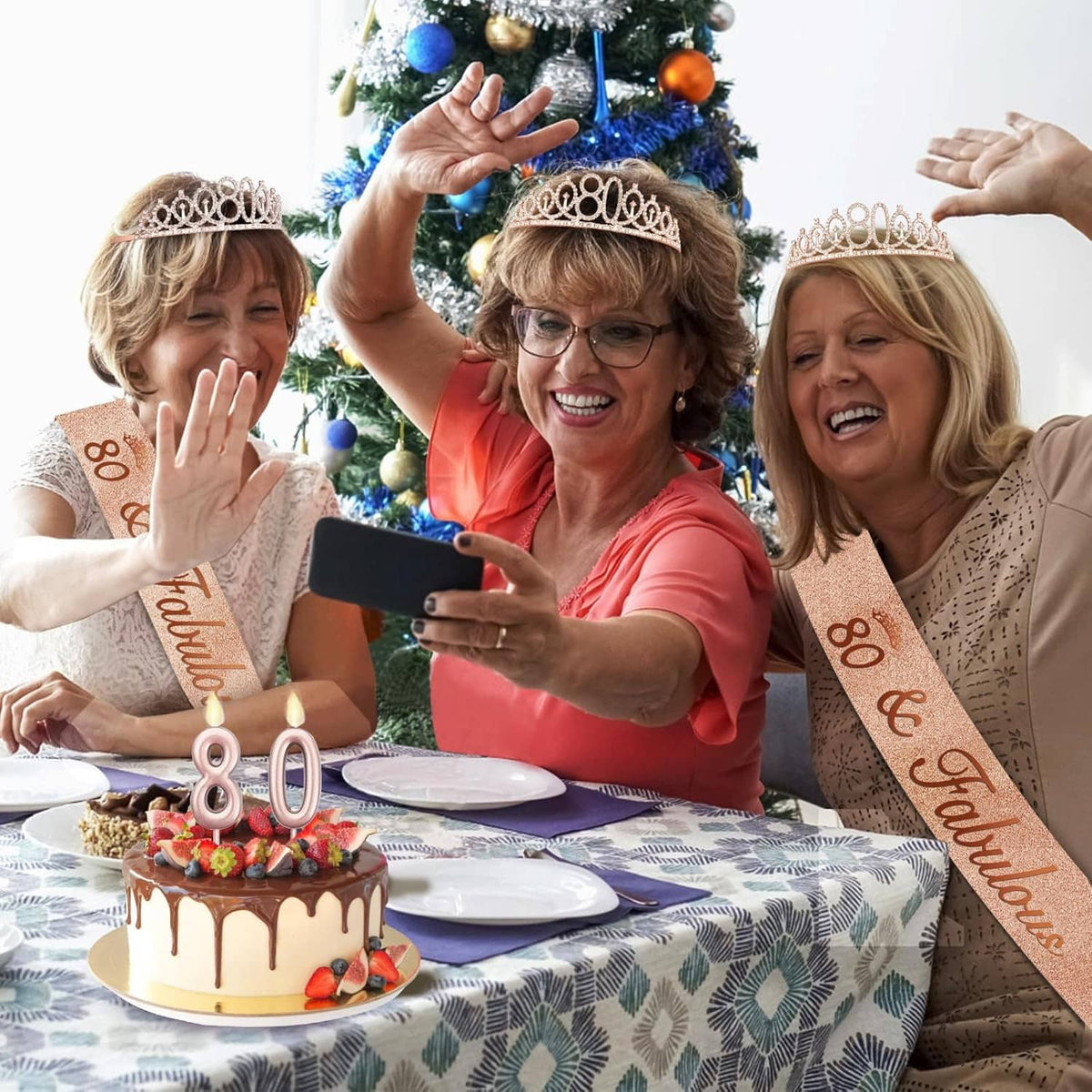 Friends celebrating with rose-gold 80 tiaras and sashes beside a small candle cake