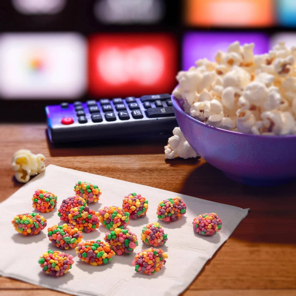 Purple bowl of rainbow gummy clusters with scattered candies on napkin