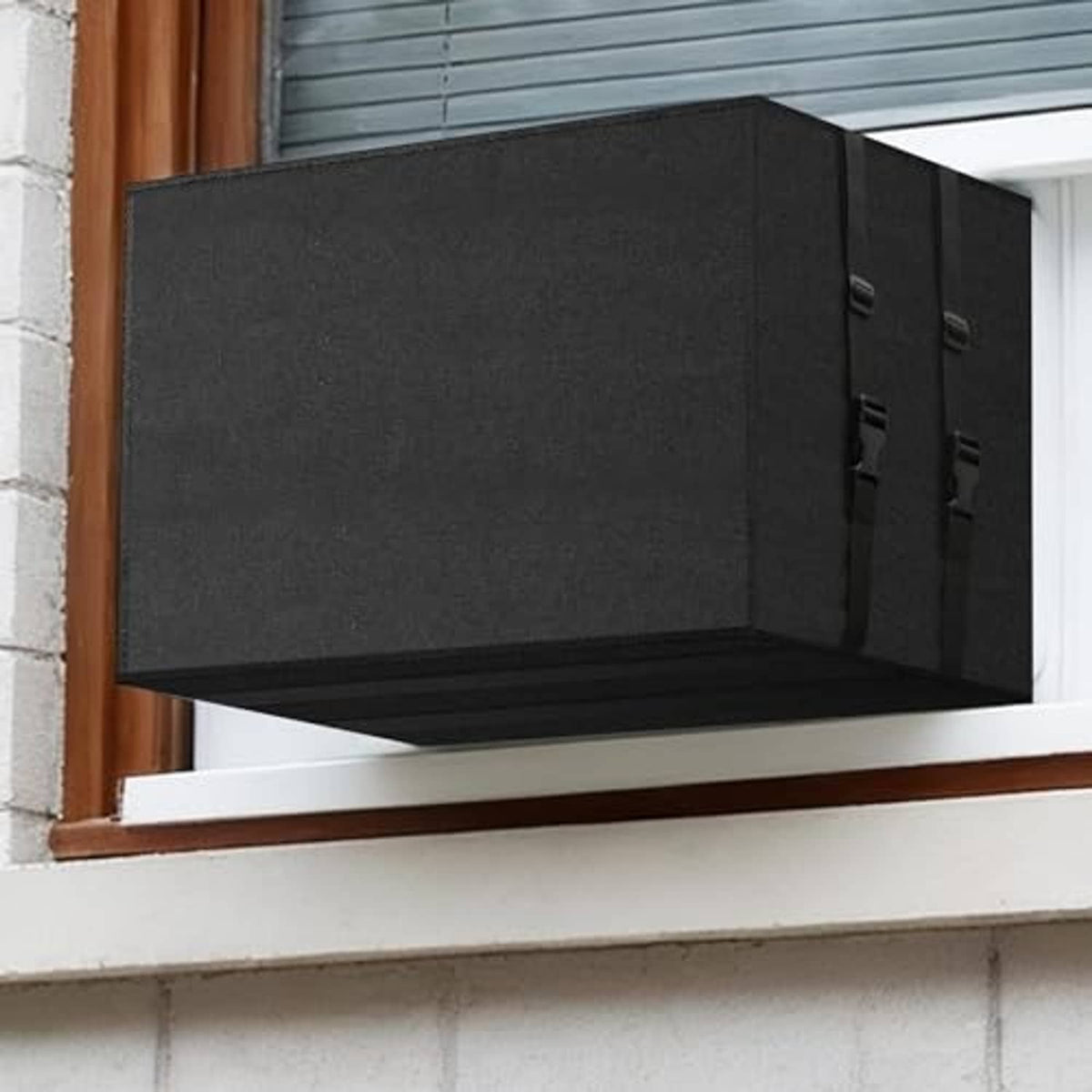 Black rectangular outdoor AC unit cover installed on a window sill with side strap panels.