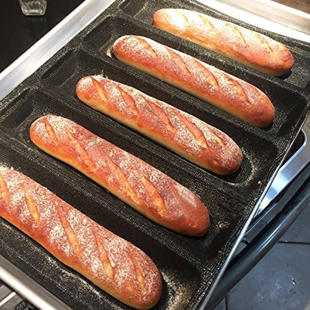 Black silicone hot dog mold holding five baked bread logs on a baking tray