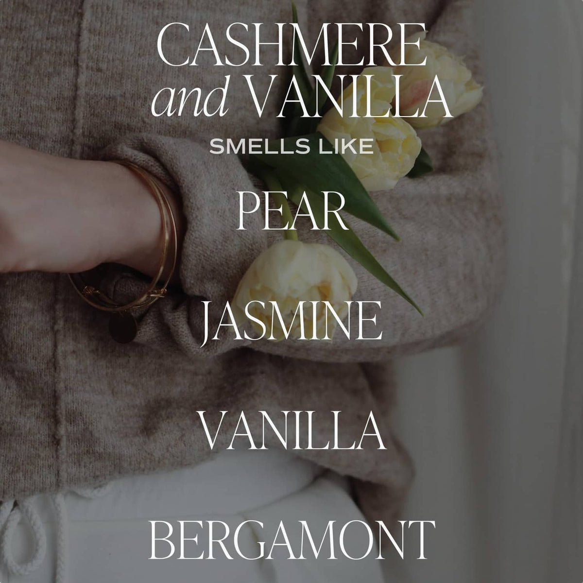 Lit cashmere and vanilla candle jar with floral label and hand holding pear and jasmine