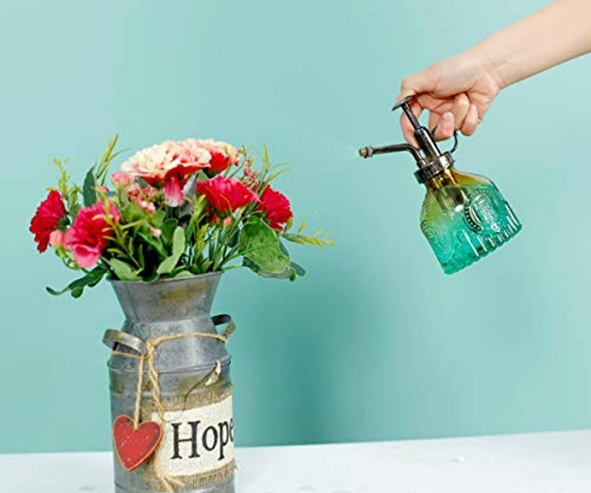 Glass plant mister bottle in teal green with black sprayer, held in a hand.