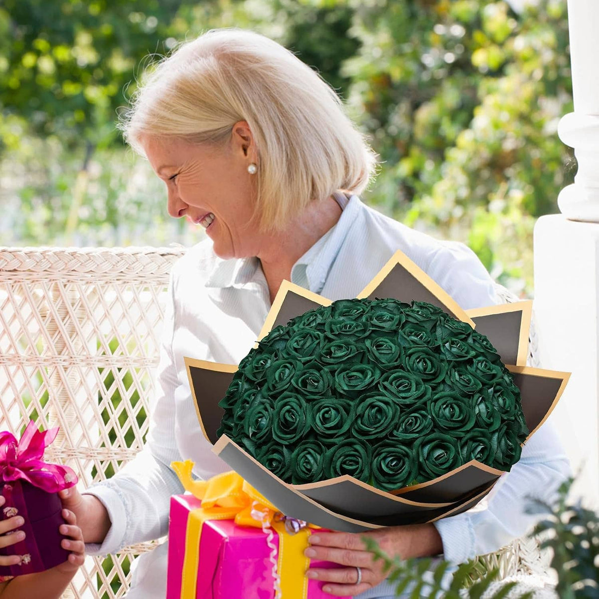 Dark green artificial rose bouquet held outdoors by a seated woman at a picnic table