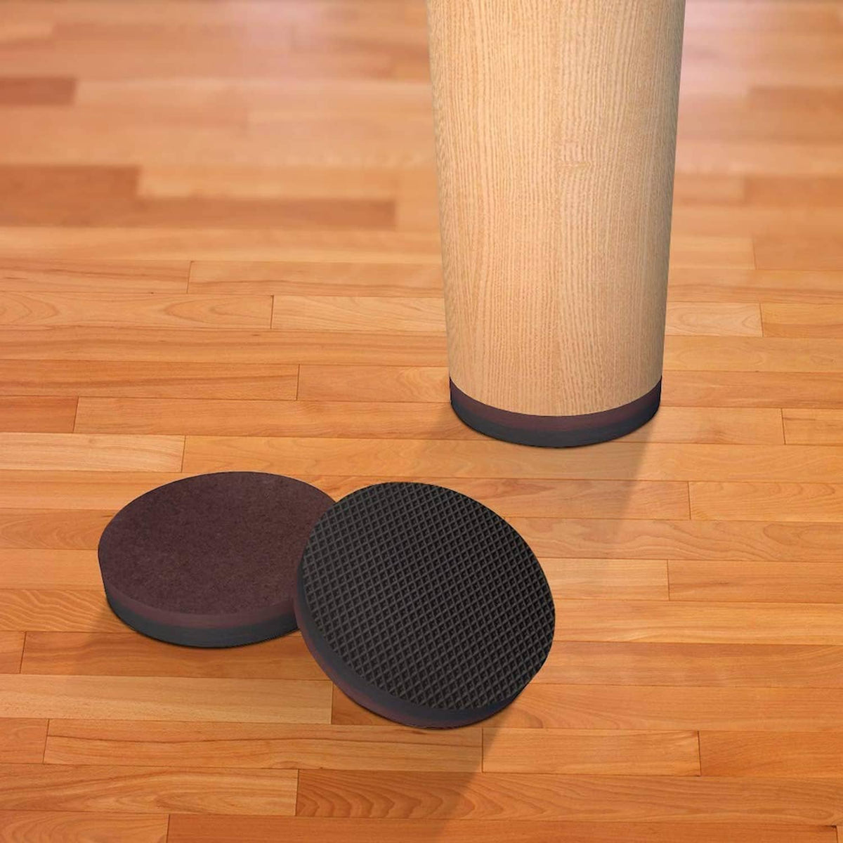 Round furniture pads under a table leg on wood floor, dark gray textured discs set
