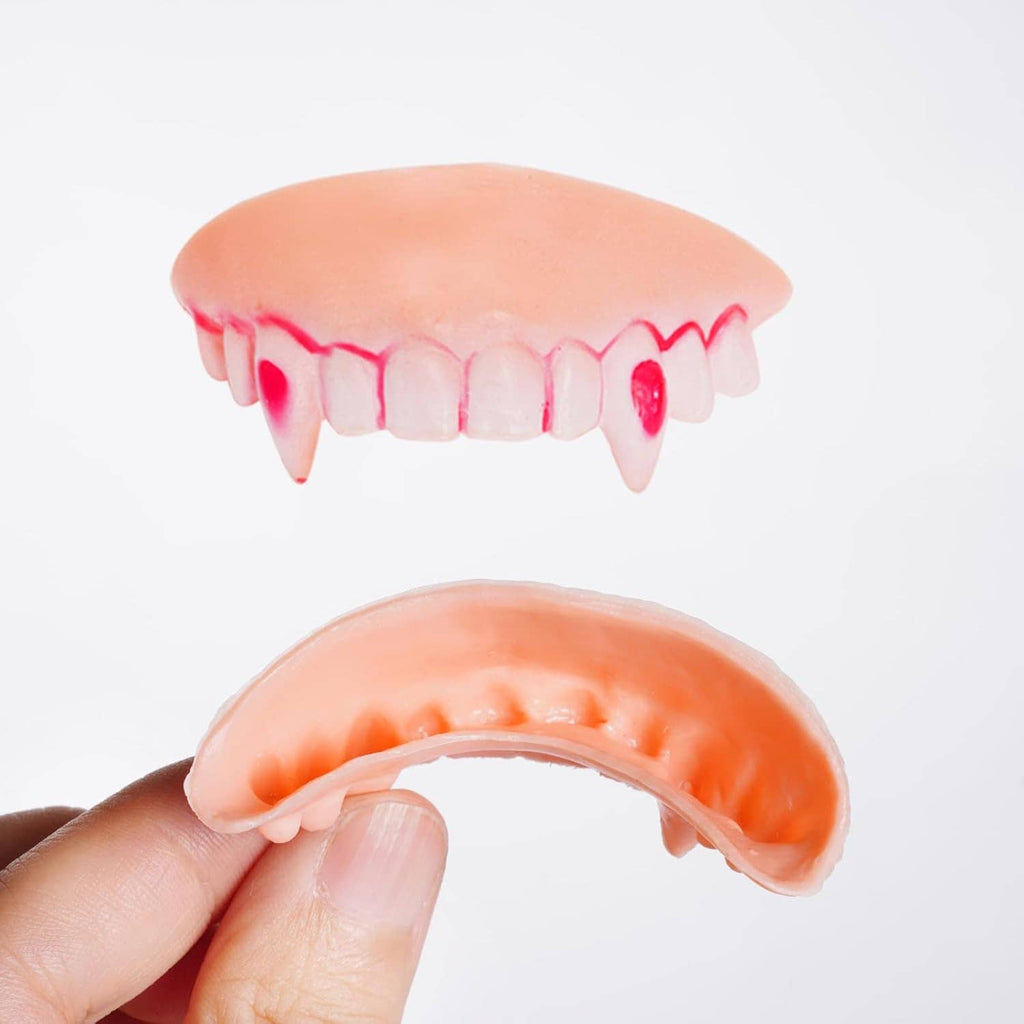 Single set of orange-pink vampire gag teeth with red-highlighted fangs and gray cap