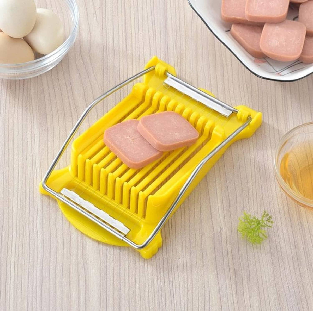 Yellow meat slicer tray with metal wires, holding pink slices over a wooden table