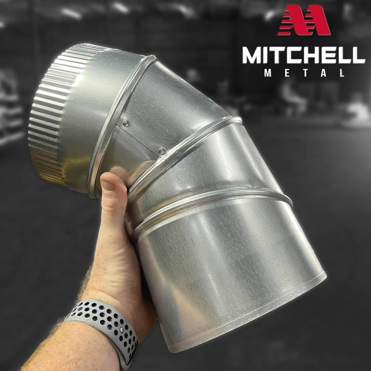 Hand holding galvanized steel 90° dryer vent elbow with ribbed ring and black flanged opening
