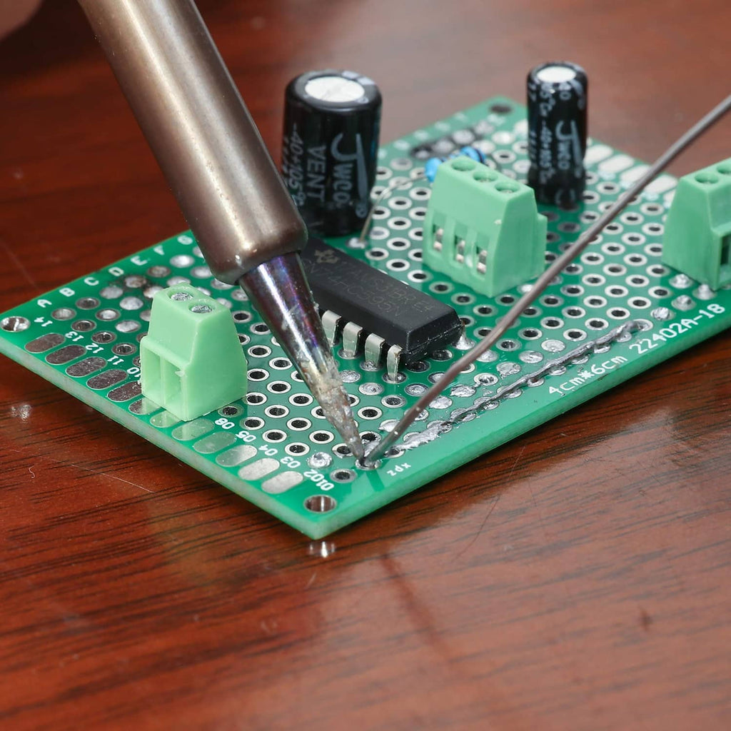 Close-up of soldering on green PCB prototyping board with components and wires