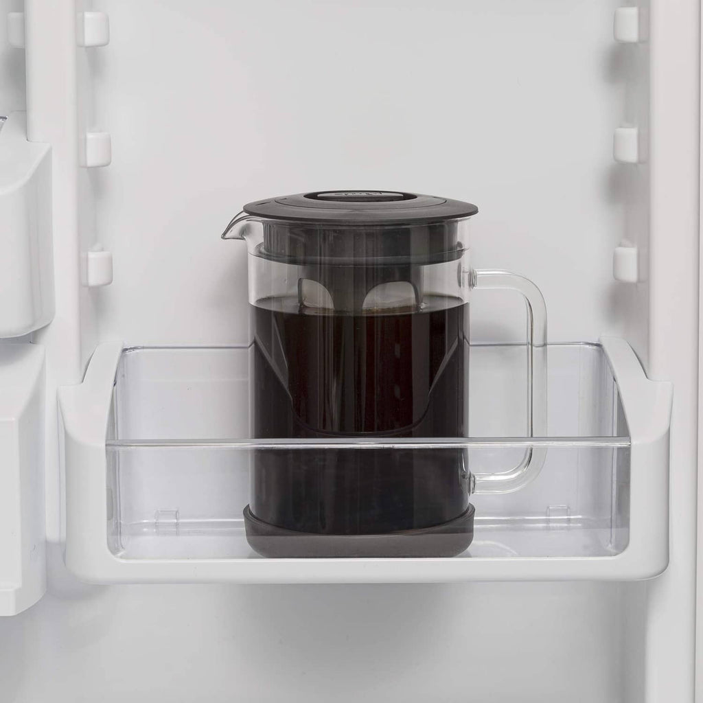 Cold brew coffee maker with black lid in refrigerator shelf, clear glass pitcher
