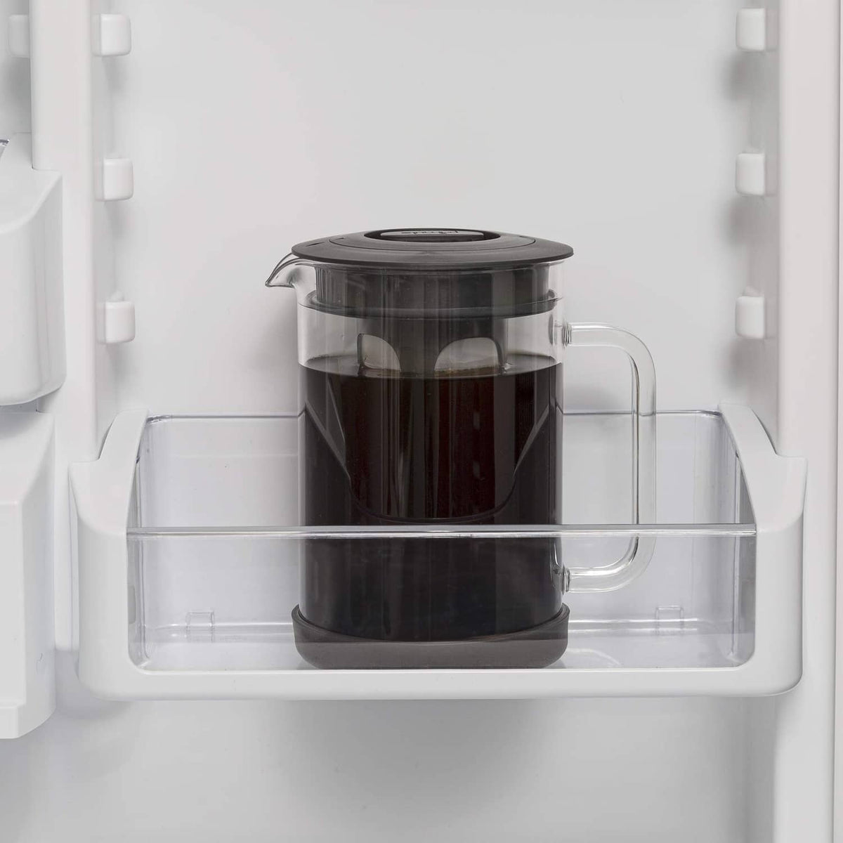 Cold brew coffee maker with black lid in refrigerator shelf, clear glass pitcher