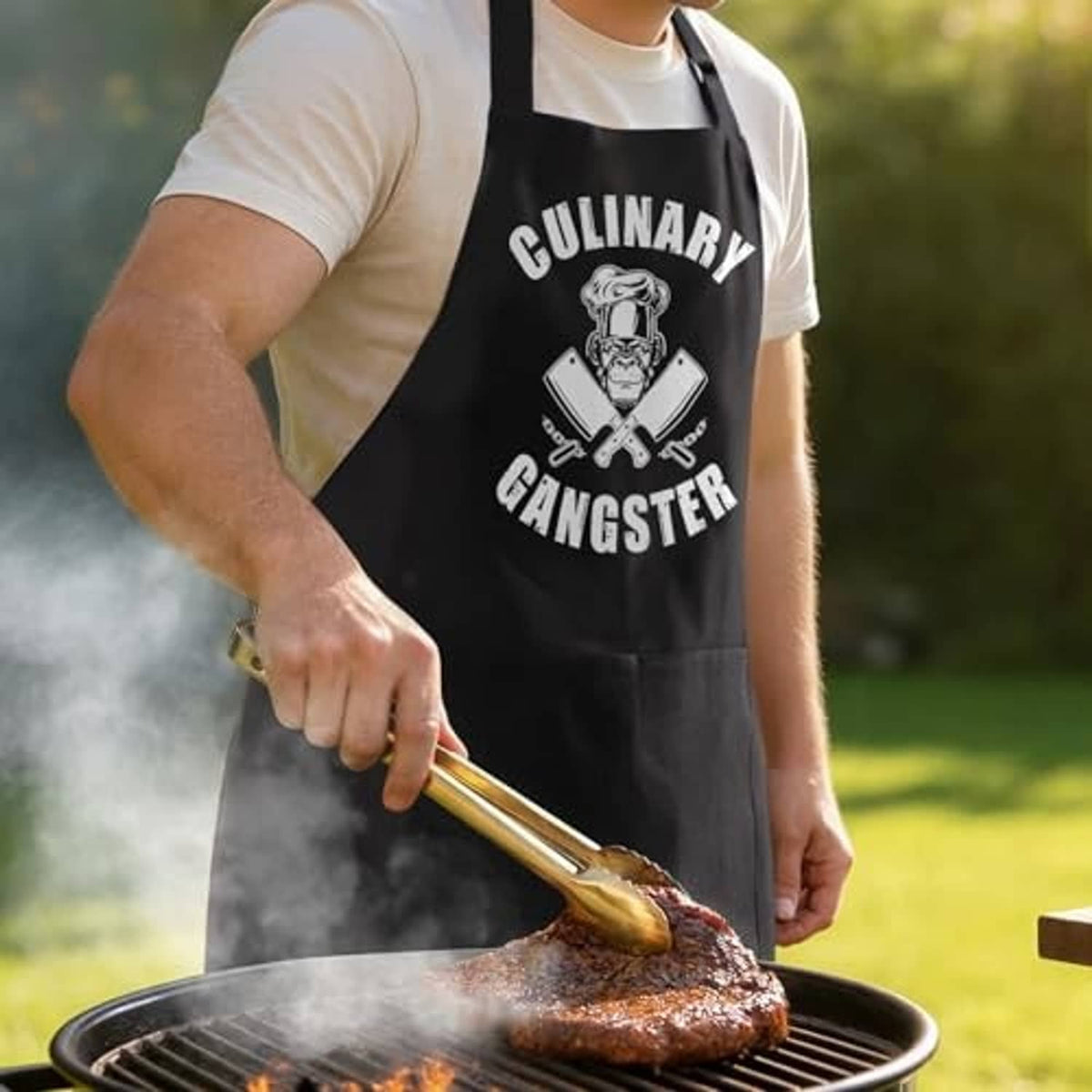 Black cooking apron with 'Culinary Gangster' logo, worn while grilling outdoors