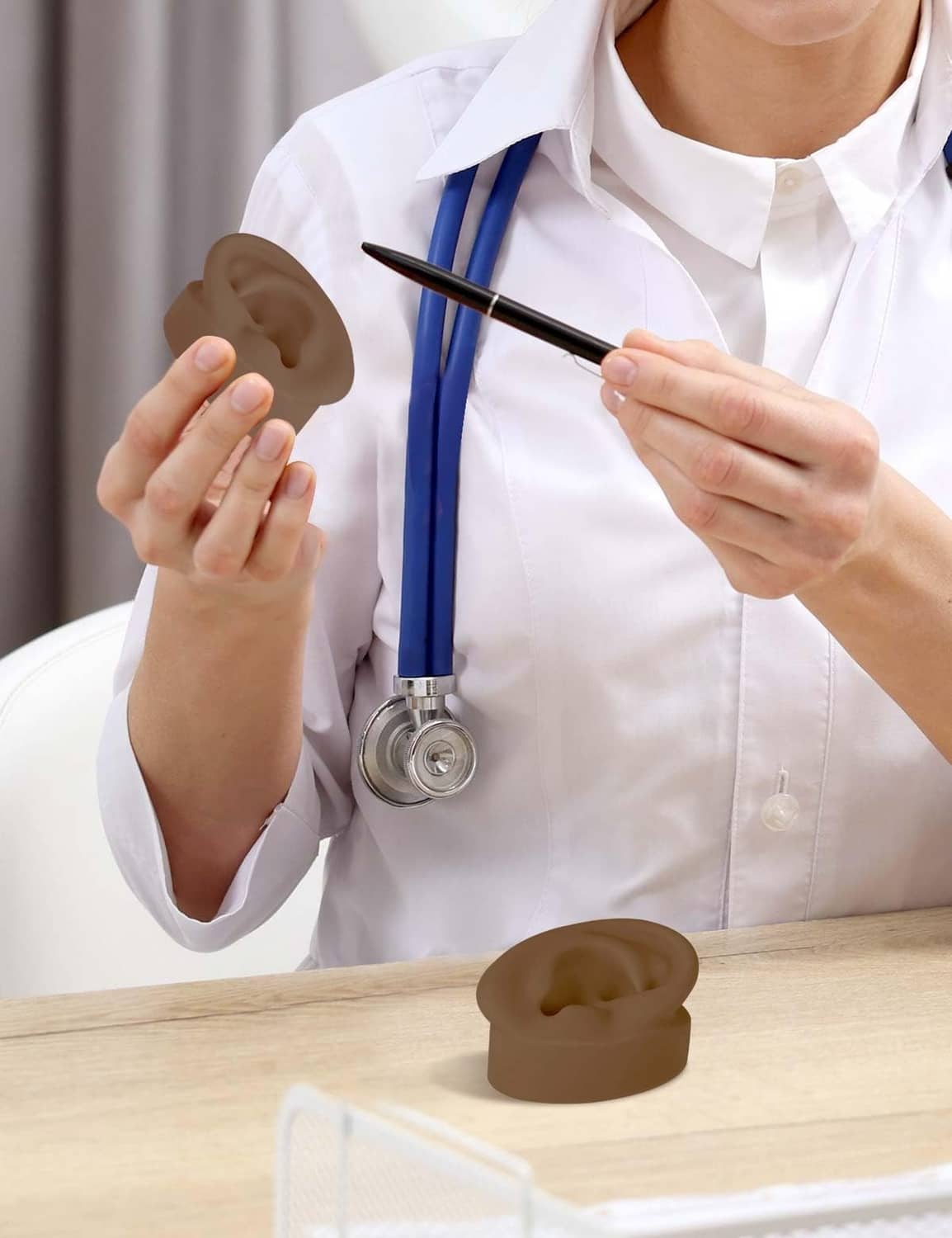 Dark brown silicone ear model on a desk while a person holds piercing tools