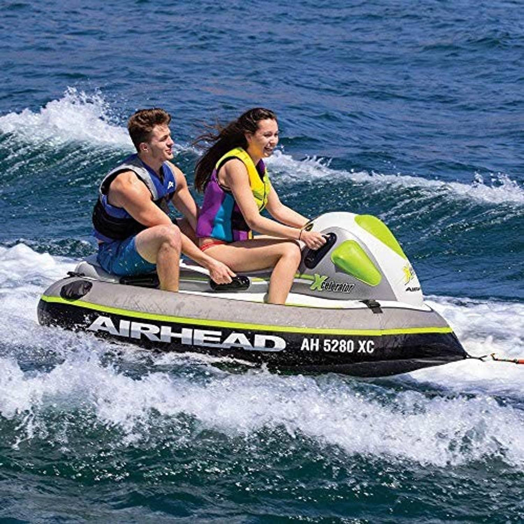 Two riders seated on a white, gray, and neon green towable tube on open water