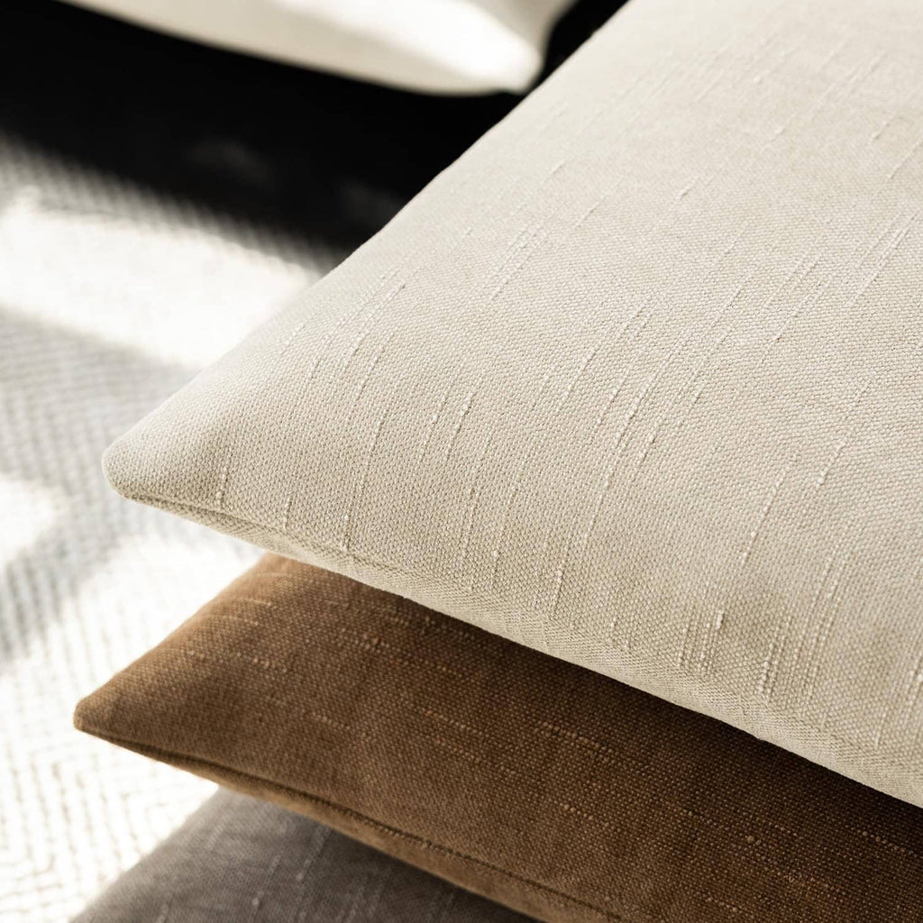 Beige chenille pillow corner with stitched edge and vertical textured thread lines.