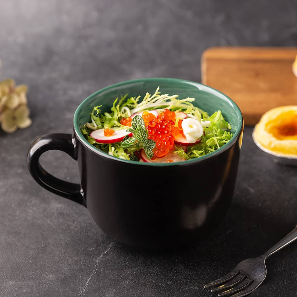 Black soup mug with handle filled with salad greens, strawberries, and sliced vegetables