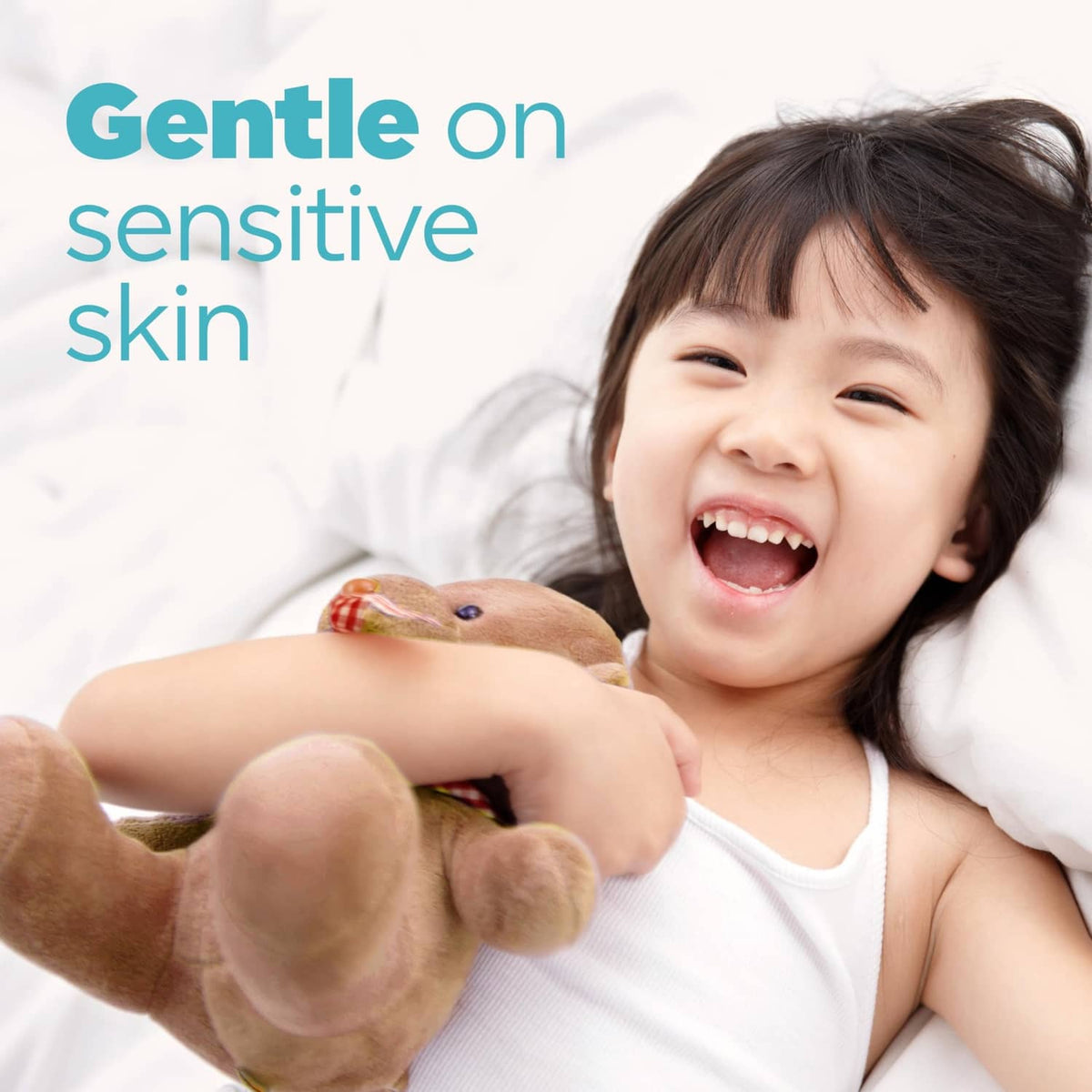 Laughing child on a bed holding a plush toy, Tide gentle detergent