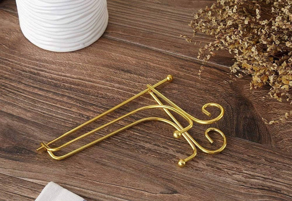 Gold metal plate stand with three swirled feet, laid diagonally on wood.