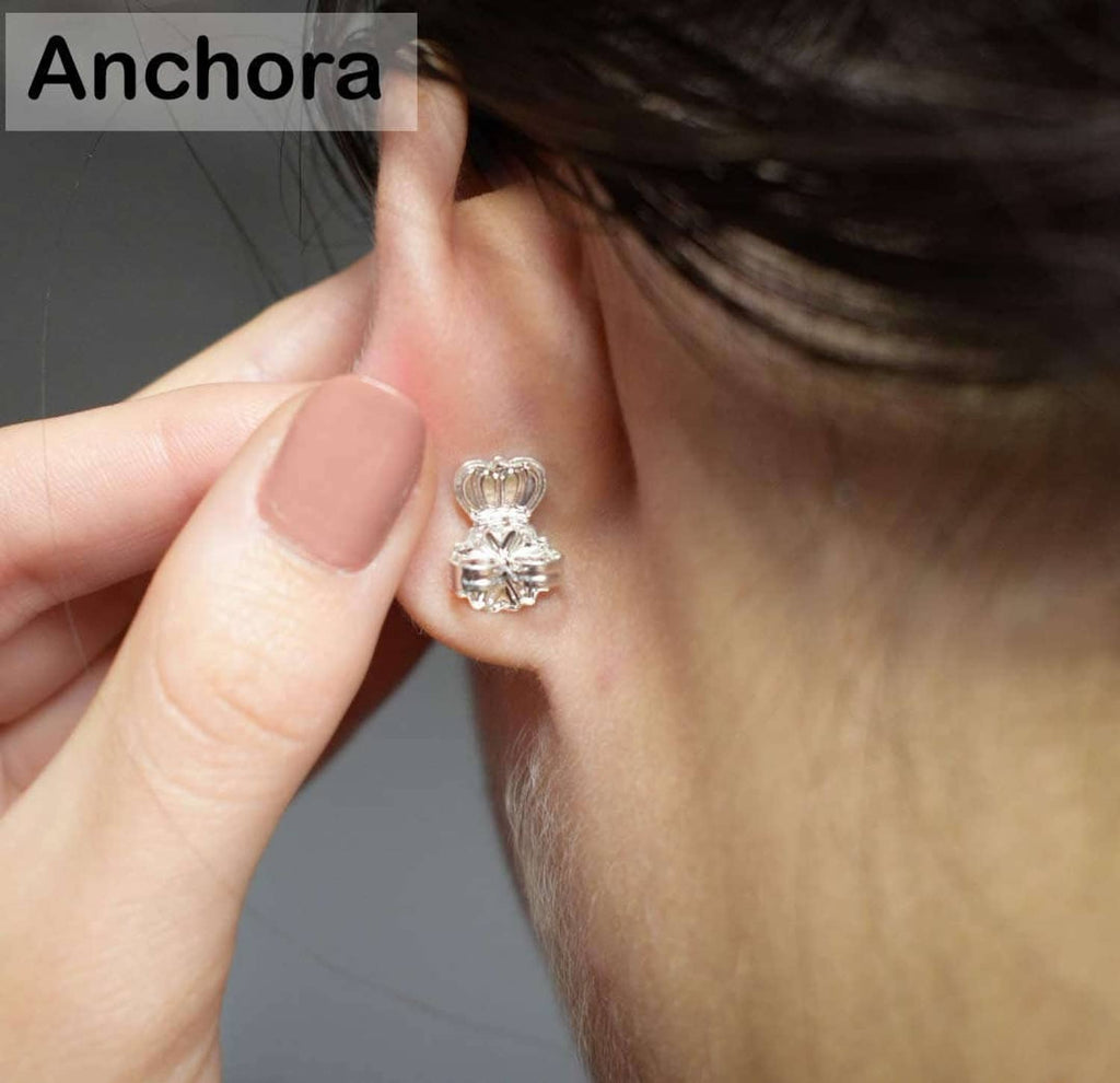 Silver earring back clip held on a finger against an earlobe
