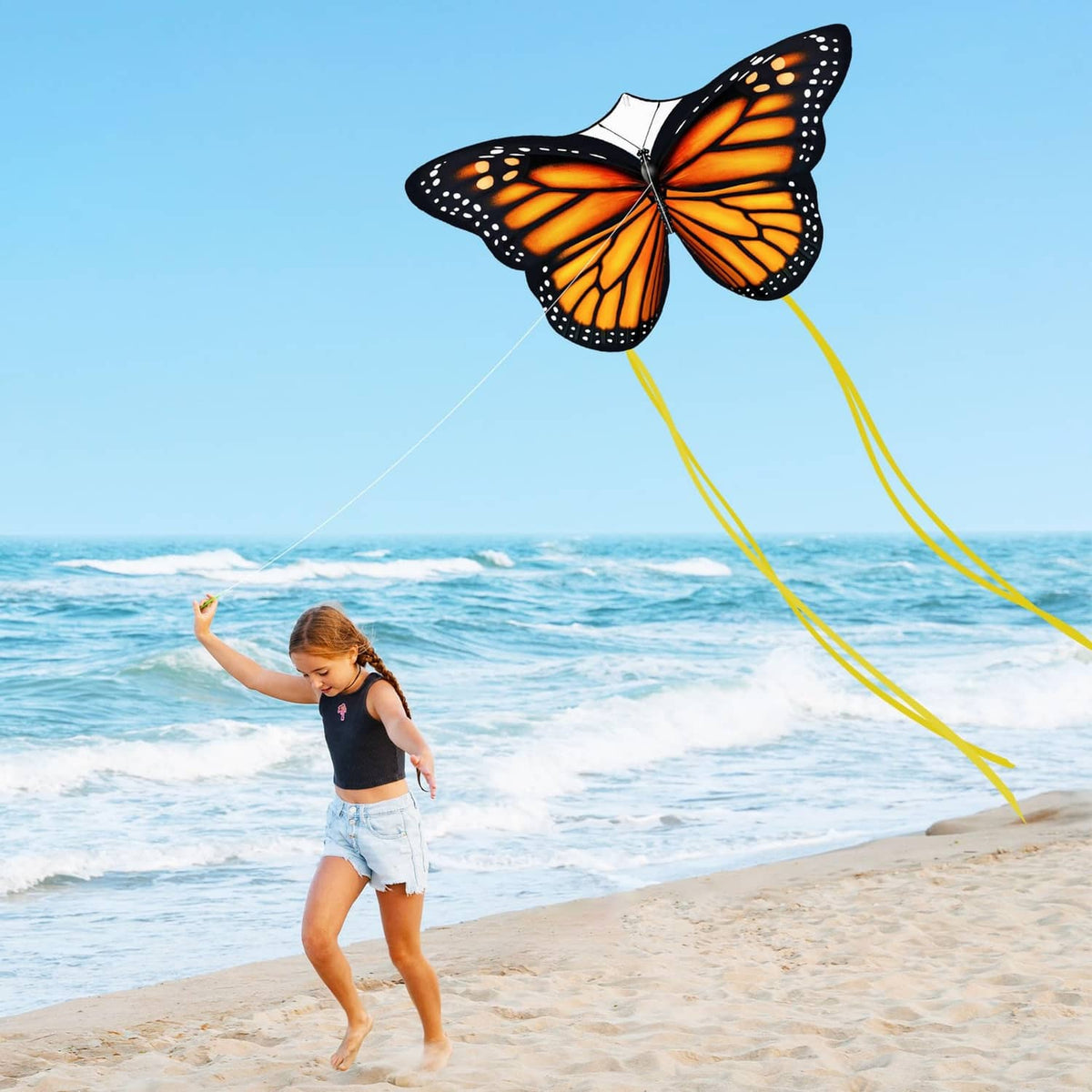 Monarch butterfly kite flying with orange wings, black dots, and long yellow ribbons